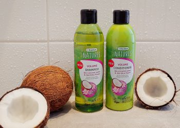Een witte badkamer met waterdruppels op de muur rechts ligt een dichte kokosnoot met een halve opengebroken kokosnoot twee flessen Kruidvat Natures volume shampoo en conditioner en rechts een halve open kokosnoot