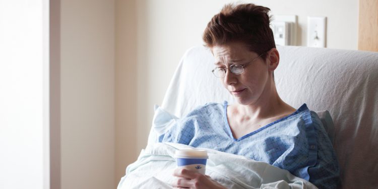 Vrouw in ziekenhuisbed met bekertje in de hand
