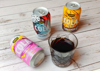Drie blikjes jumbo cola special edition met een glas cola ernaast