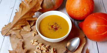 Pompoensoep in een wit bakje. Met pompoenen, herfstbladeren en walnoten op een houten plank